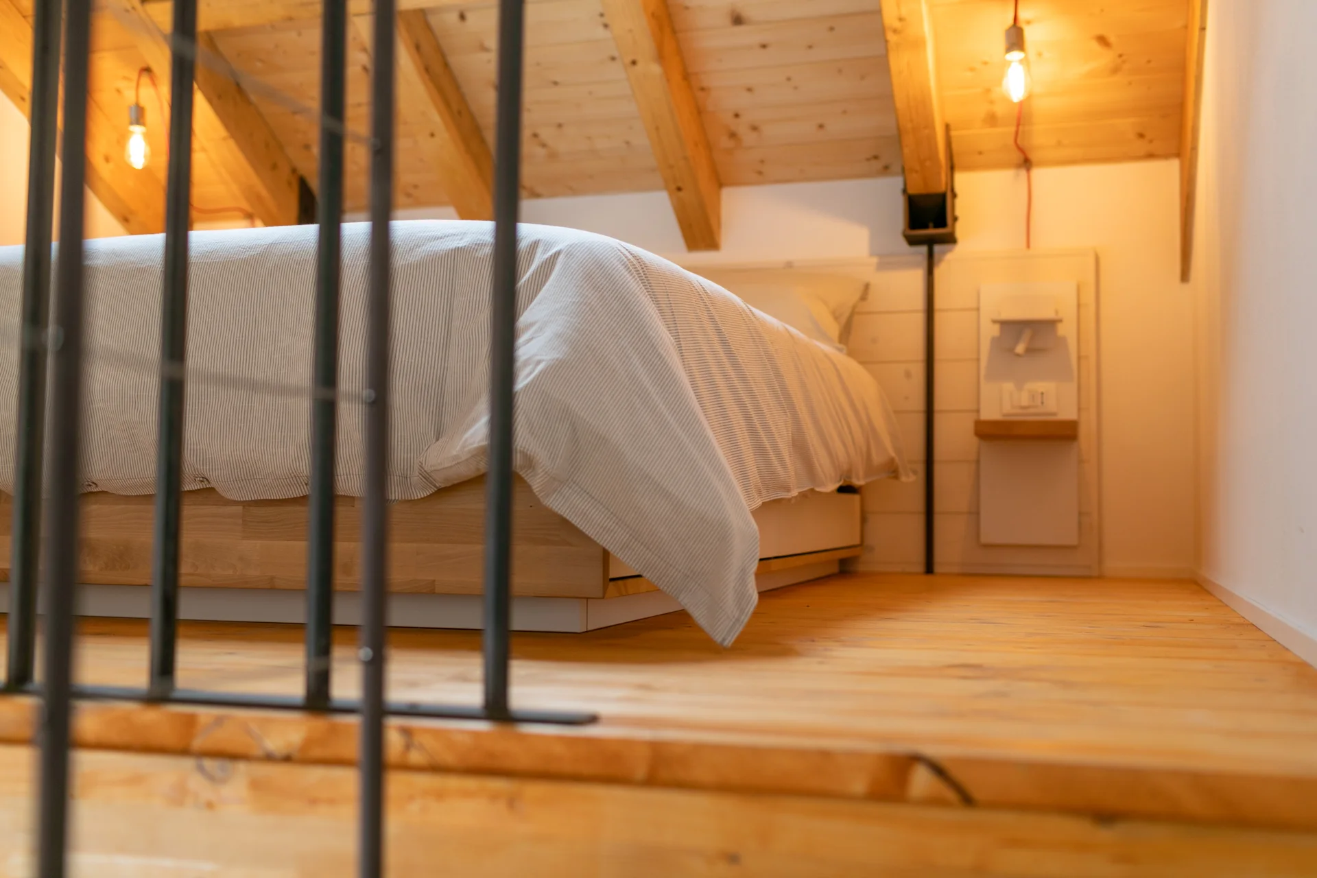 Soppalco con letto, travi in legno e ringhiera scura